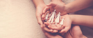 A group of three peoples hands are together, holding a paper cutout of a family