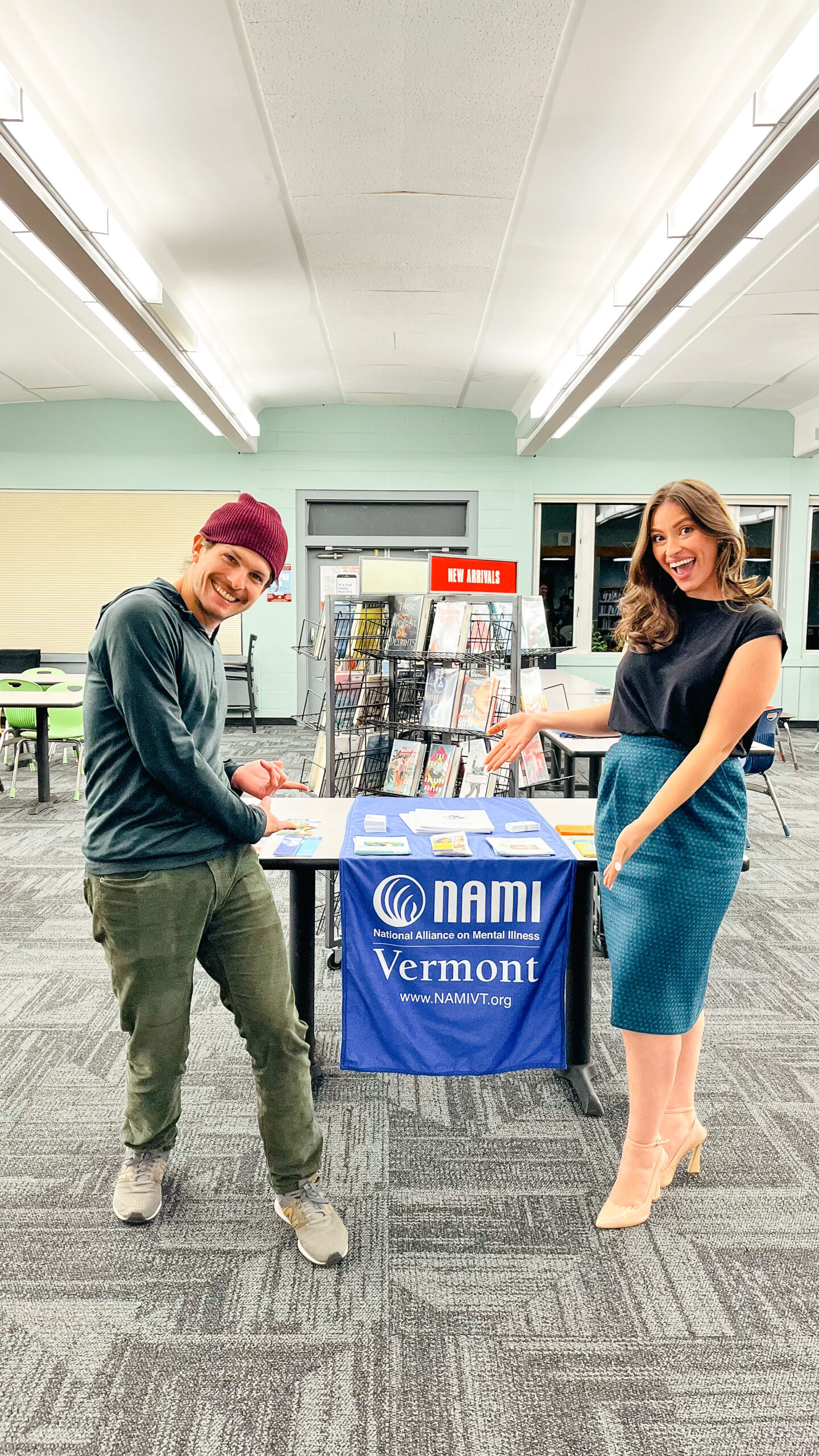 smiling young man and woman point at table with NAMI Vermont sign