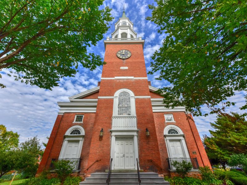 tall brick church surrounded by green trees. blue sky background with white clouds